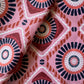 The Rekka Bottom from Lemlem's Malia Bikini features adjustable ties with a geometric pattern in pink, red, white, and navy, displaying circular motifs and diamond shapes.