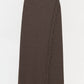 The Casey Knit Skirt by Simkhai is a long, ribbed dark brown midi skirt made from a luxurious wool-cashmere blend, featuring fringe trim along its stylish faux-wrap front and hem, shown against a plain white background.