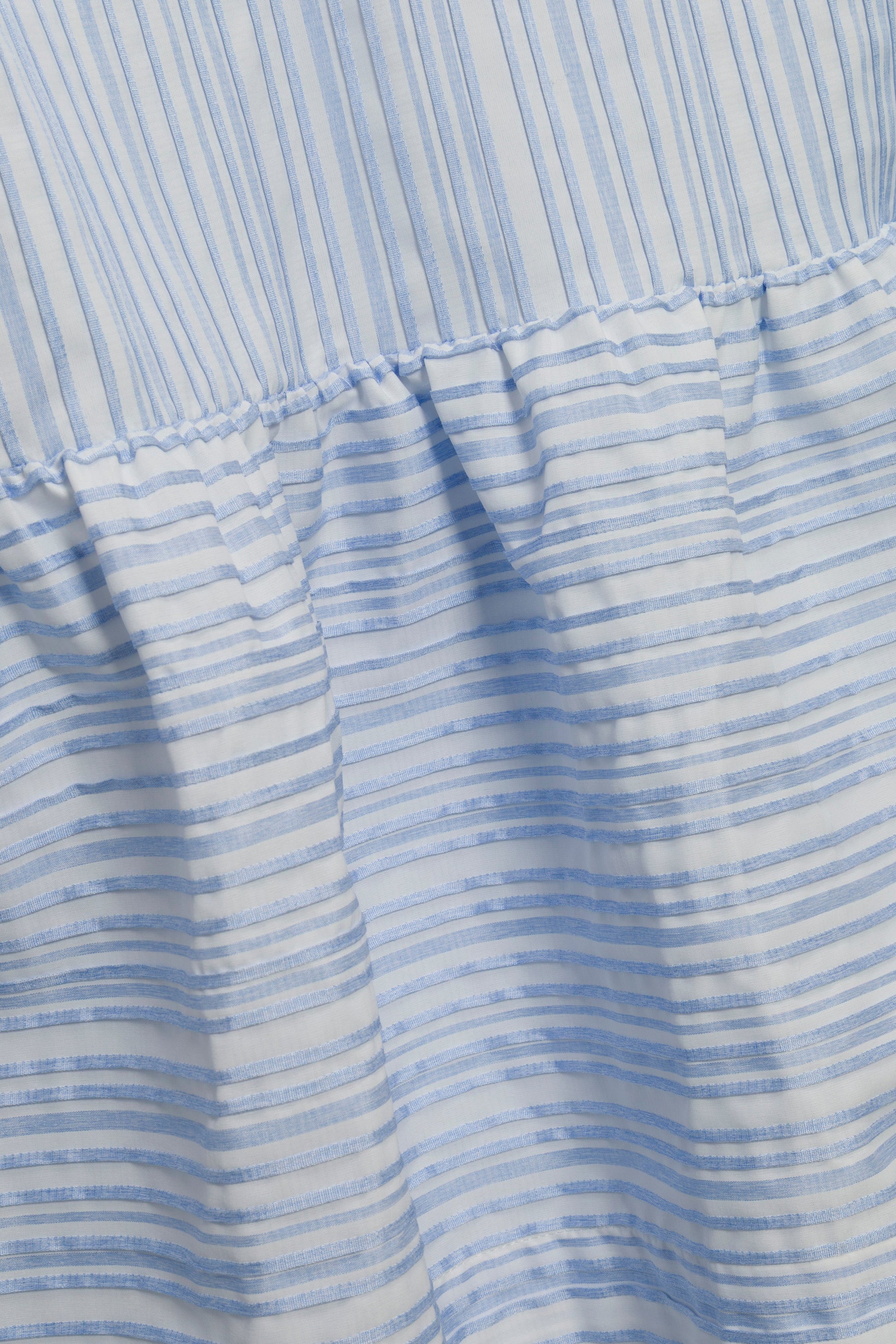 Close-up of light blue and white striped fabric with gathered seams and varied line thickness, featured on the Simkhai Cris Short Sleeve Shirt Dress.