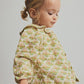 A young toddler girl with light brown hair in pigtails, wearing the Cozmo Baby Girls’ Iris Printed Blouse and mustard corduroy pants, stands against a neutral background.