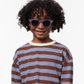 A child with curly hair smiles at the camera while wearing IZIPIZI Kids’ #C Polarized Sunglasses and a long-sleeve shirt featuring brown, blue, and white stripes, standing against a plain white background.
