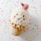 The MON AMI Izzy Ice Cream Chime Toy by Mon Ami is a plush toy designed to resemble an ice cream cone, featuring a cheerful smiley face, a pink cherry on top, and colorful sprinkles against a white backdrop. This sensory toy enchants children with its gentle chime sound, making it an ideal activity toy for babies to enjoy endless playtime fun.