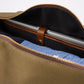 A laptop secured inside a partially open brown Bennett Winch Canvas Weekender bag, crafted from waterproof canvas, with folded blue clothing visible beneath it.