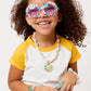 Smiling child with curly hair wears Super Smalls Mermaid Splash & Sparkle Gemify Sunglasses & Case, yellow and white top, chunky necklace, bracelets, and holds a small purple purse—great inspiration for kids’ crafting or DIY gem projects.