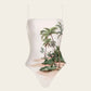 The Durazno Arena One Piece by Agua By Agua Bendita is a white swimsuit with thin straps, made from recycled polyester, featuring a tropical beach print and UPF 50 sun protection—perfect for stylish days by the water.