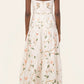 A woman is seen from behind wearing the Lima Navegante Maxi Dress by Agua By Agua Bendita, featuring a floral pattern, a fitted bodice, and hand-embroidered straps.