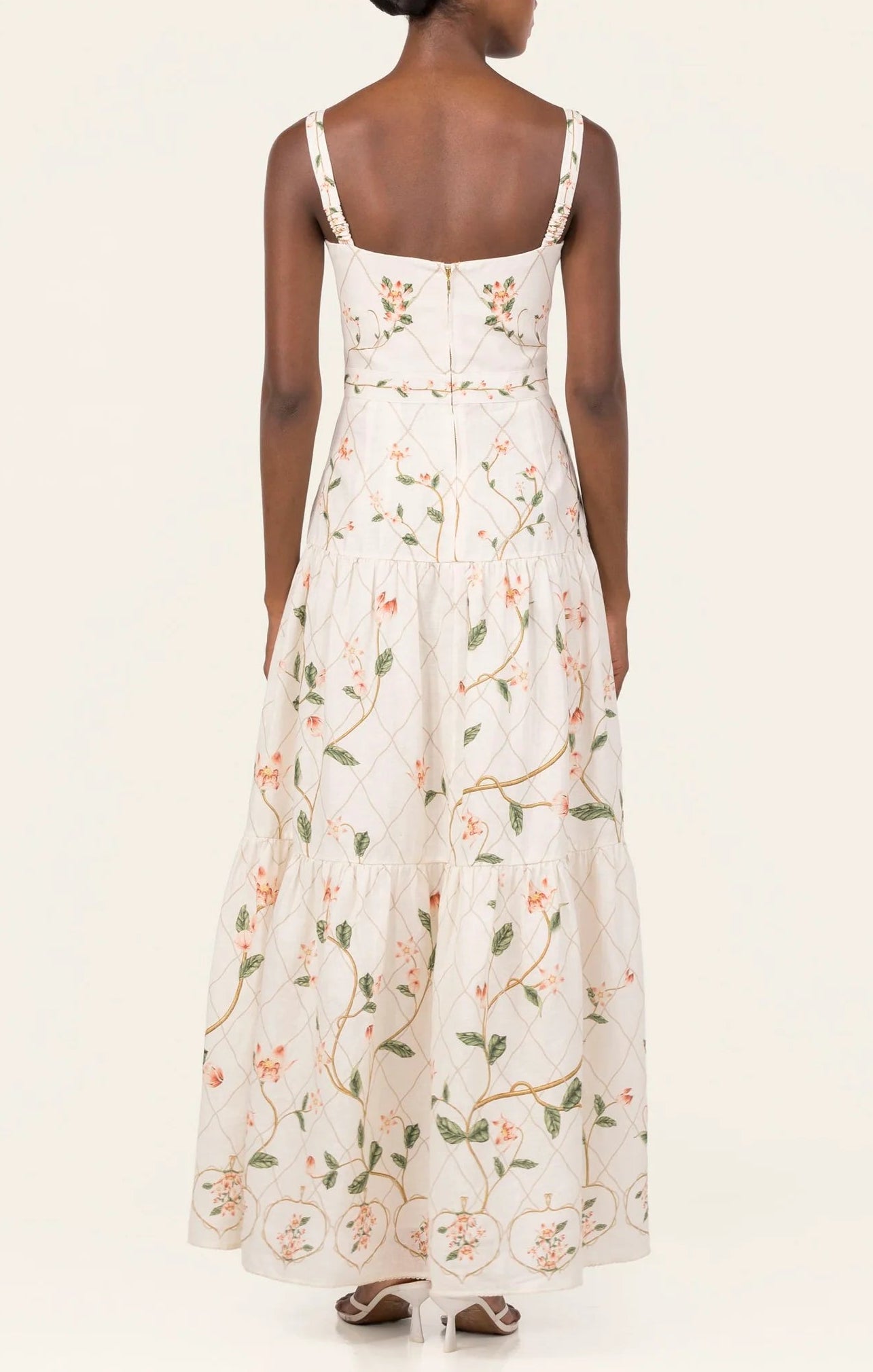 A woman is seen from behind wearing the Lima Navegante Maxi Dress by Agua By Agua Bendita, featuring a floral pattern, a fitted bodice, and hand-embroidered straps.