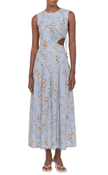A person wearing the Otono Navegante Midi Dress by Agua By Agua Bendita—a sleeveless, light blue floral dress with side cutouts—paired with white sandals.