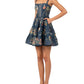 Agua By Agua Bendita Lima Mini Dress in dark blue poplin with hand-embroidered floral print, a square neckline, and a tiered skirt, shown with one hand in a pocket.
