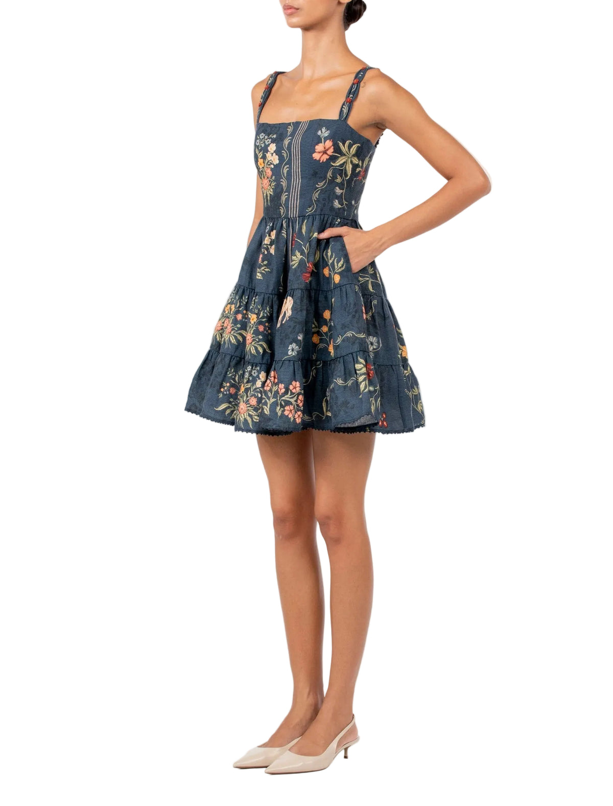 Agua By Agua Bendita Lima Mini Dress in dark blue poplin with hand-embroidered floral print, a square neckline, and a tiered skirt, shown with one hand in a pocket.