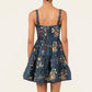 Back view of the Agua By Agua Bendita Lima Mini Dress, a sleeveless navy blue poplin dress with a tiered skirt, hand-embroidered floral print, and red rosettes on the straps.