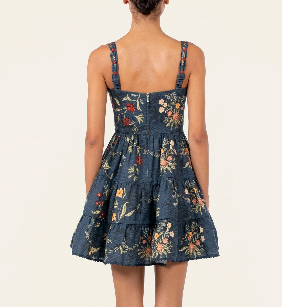 Back view of the Agua By Agua Bendita Lima Mini Dress, a sleeveless navy blue poplin dress with a tiered skirt, hand-embroidered floral print, and red rosettes on the straps.