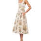 A person wearing an Agua By Agua Bendita Pistilo Dress, featuring a sleeveless, cream-based floral print midi silhouette with a square neckline and side pockets.