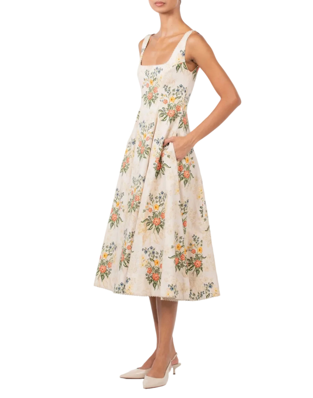 A person wearing an Agua By Agua Bendita Pistilo Dress, featuring a sleeveless, cream-based floral print midi silhouette with a square neckline and side pockets.