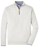 A cream-colored "Peter Millar Autumn Crest Quarter-Zip Suede Trim" sweater in a classic fit is layered over a blue button-up shirt, offering both breathable comfort and style.