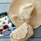 The Mar Y Sol Jane Hat and a matching woven clutch are placed next to an open magazine on a wooden surface.