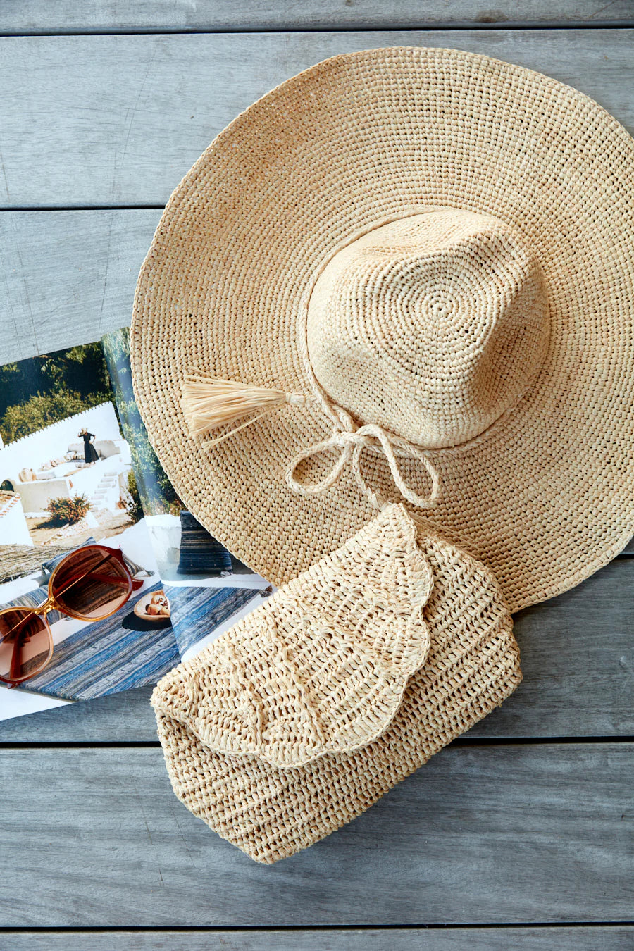 The Mar Y Sol Jane Hat and a matching woven clutch are placed next to an open magazine on a wooden surface.