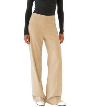 A person wearing the Callas Milano Jacky Pant—high-rise, wide-leg beige pants—paired with a fitted dark long-sleeve top and white shoes, standing against a plain background.