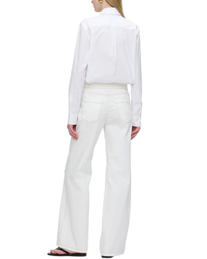 A person stands facing away, wearing a white long-sleeve shirt and Callas Milano's Jane Pant—high rise, wide-leg organic cotton jeans with back pockets—paired with black sandals.