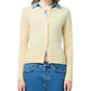 A person wears a light yellow Guest in Residence Jane Cardigan over a blue collared shirt with blue high-waisted jeans.