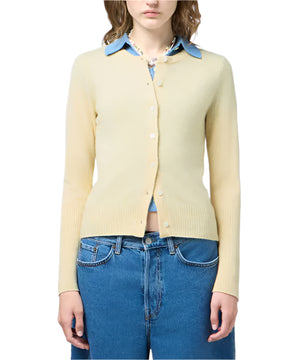 A person wears a light yellow Guest in Residence Jane Cardigan over a blue collared shirt with blue high-waisted jeans.