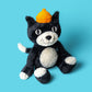 A 24" Jellycat Jack Huge tuxedo cat toy by Jellycat, featuring soft black and white fur and a yellow acorn-shaped hat, sits against a bright blue background.