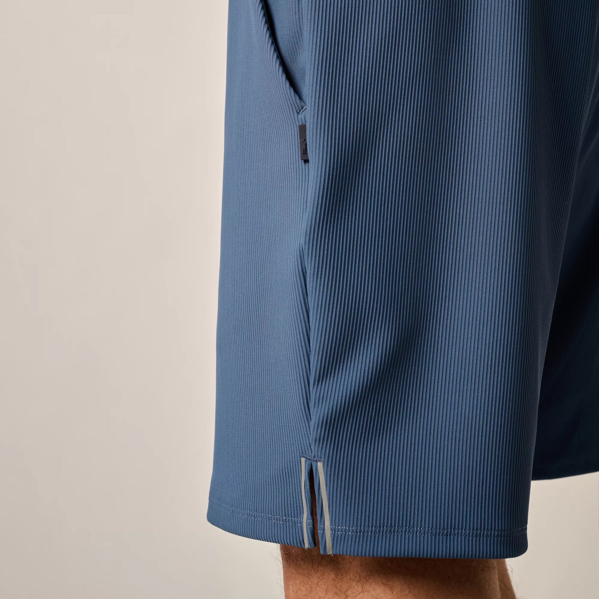 Close-up of a person wearing the Johnnie-O Hoppin Shorts, featuring blue rib-knit fabric and a side seam pocket zipper partially visible.