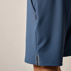 Close-up of a person wearing the Johnnie-O Hoppin Shorts, featuring blue rib-knit fabric and a side seam pocket zipper partially visible.