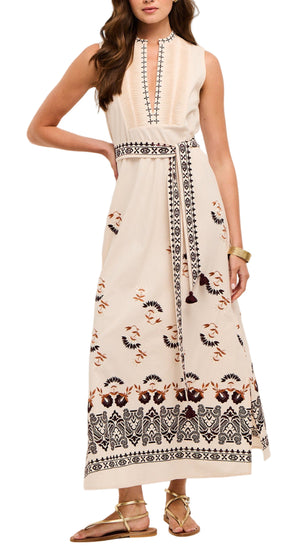 A woman wearing the Figue Joan Dress, a sleeveless cream maxi with embroidered patterns and a belted waist, paired with gold sandals.