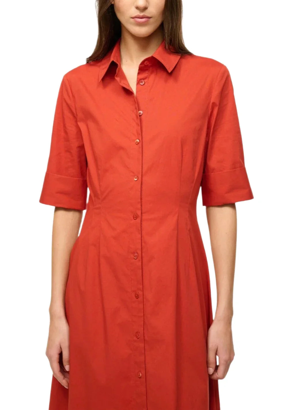 A person wearing an orange Staud Joan Maxi Dress, crafted from stretchy cotton poplin and featuring a collar and short sleeves, stands confidently against a white background.