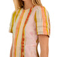 A woman models the Casey Dress by Hunter Bell NYC, a versatile sheath midi featuring vertical multicolored stripes in orange, yellow, pink, and blue. Only her upper body and part of her face are visible.