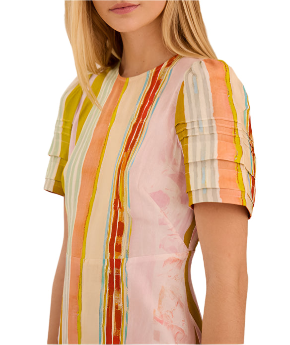A woman models the Casey Dress by Hunter Bell NYC, a versatile sheath midi featuring vertical multicolored stripes in orange, yellow, pink, and blue. Only her upper body and part of her face are visible.