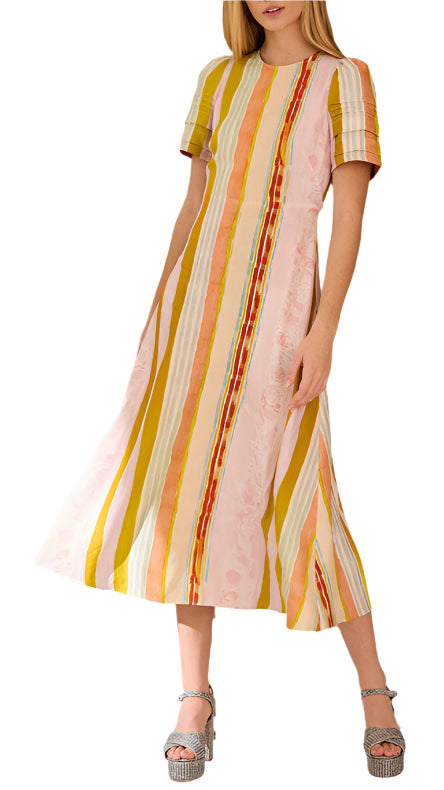 A woman models the Hunter Bell NYC Casey Dress, a versatile ankle-length piece with short sleeves and yellow, pink, and orange vertical stripes, styled with silver platform heels.