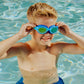 A young boy in a pool smiles as he adjusts his blue Bling2O Kids' Jurassic Dive Goggles.