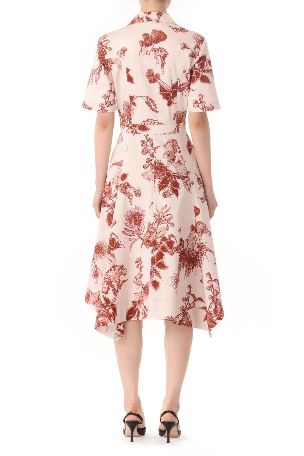 A person wearing a knee-length, short-sleeve, Jason Wu Collection Forest Floral Shirtdress with handkerchief hem, viewed from the back, standing in black heeled shoes.