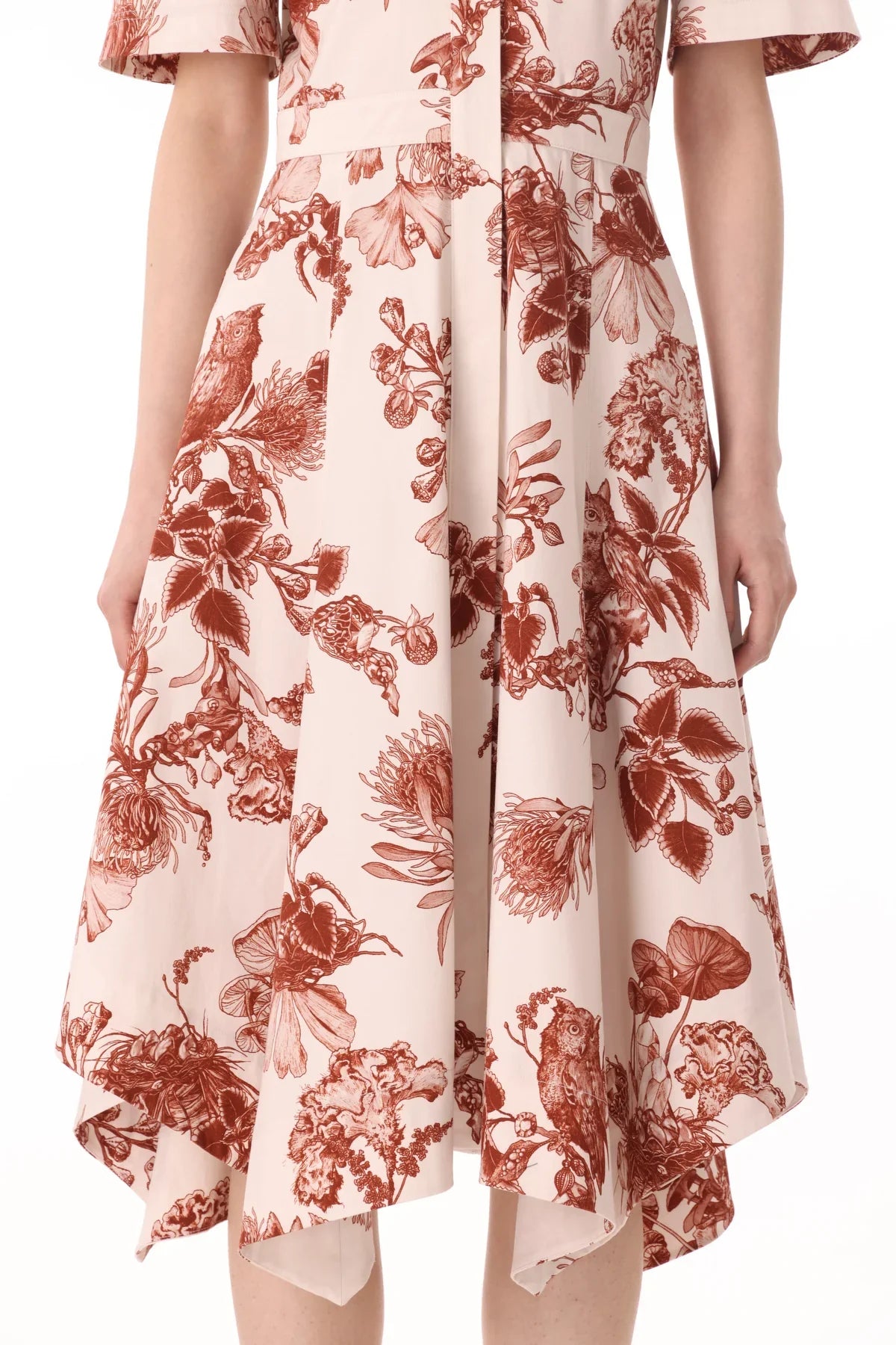 A person wearing a knee-length, cream-colored dress with brown floral patterns. The Jason Wu Collection Forest Floral Shirtdress by Jason Wu Collection features short sleeves and an asymmetrical handkerchief hemline.