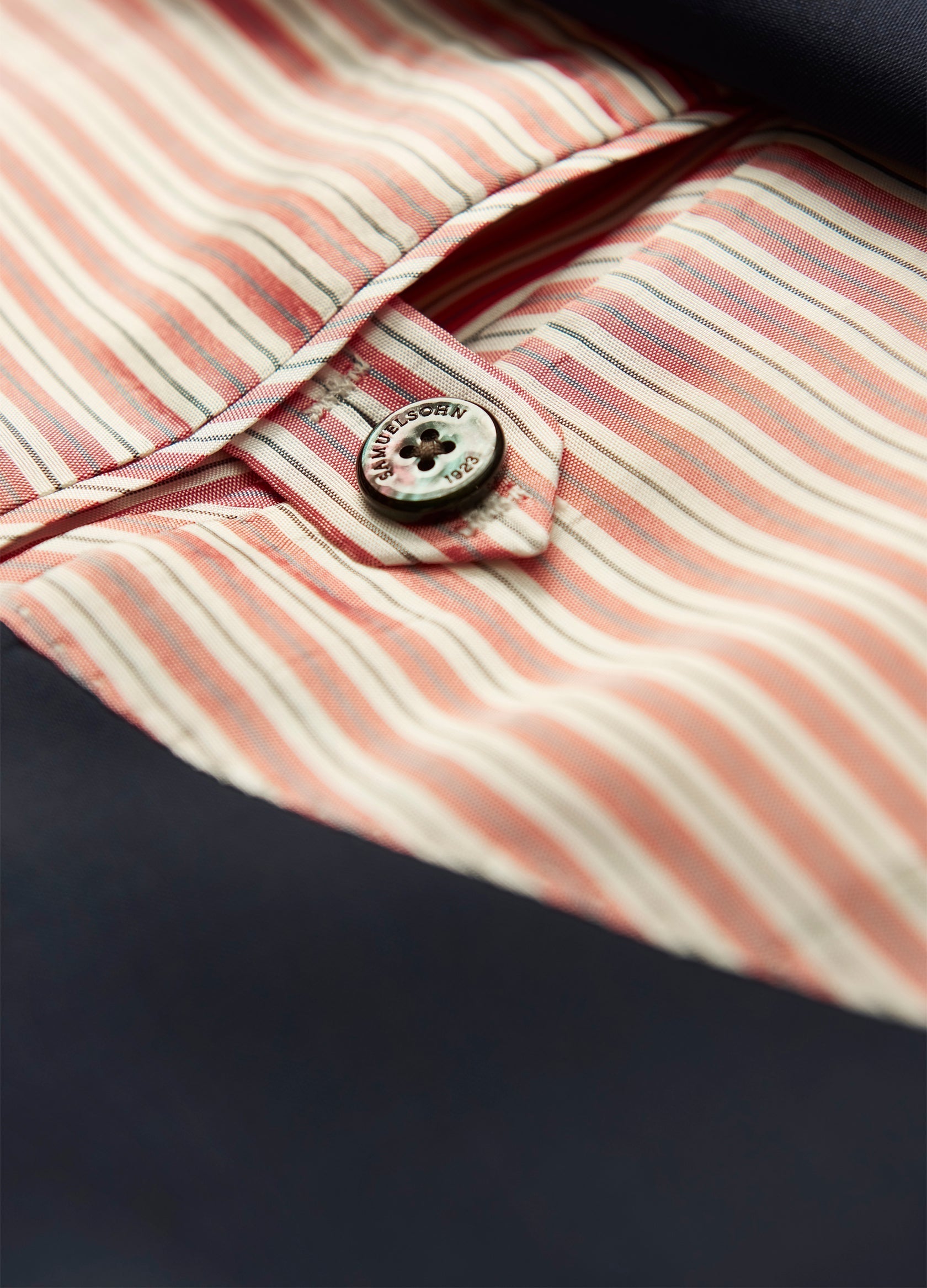 Close-up of a button on a red and beige striped shirt under a Samuelsohn Garner Revenge Poplin Blazer, highlighting the texture and details of the Super 150s Wool fabric.