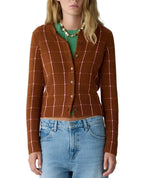 A woman wearing the Guest in Residence Jane Checker Cardigan in brown over a green top, paired with light blue jeans.