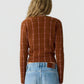 A person with long wavy blonde hair is shown from the back against a plain light background, wearing the Jane Checker Cardigan by Guest in Residence in brown cashmere, paired with light blue jeans.