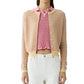 A woman wears the Guest in Residence Pebble Stripe Jane Cardigan over a pink ruffled top and white pants, standing against a white background.