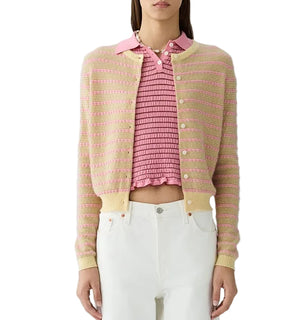 A woman wears the Guest in Residence Pebble Stripe Jane Cardigan over a pink ruffled top and white pants, standing against a white background.