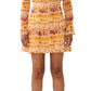 A person elegantly wearing a Jason Wu Printed Silk Crinkle Chiffon Dress with an ombre floral design, featuring smocked waist and long sleeves in yellow-orange tones, paired gracefully with black ankle boots.