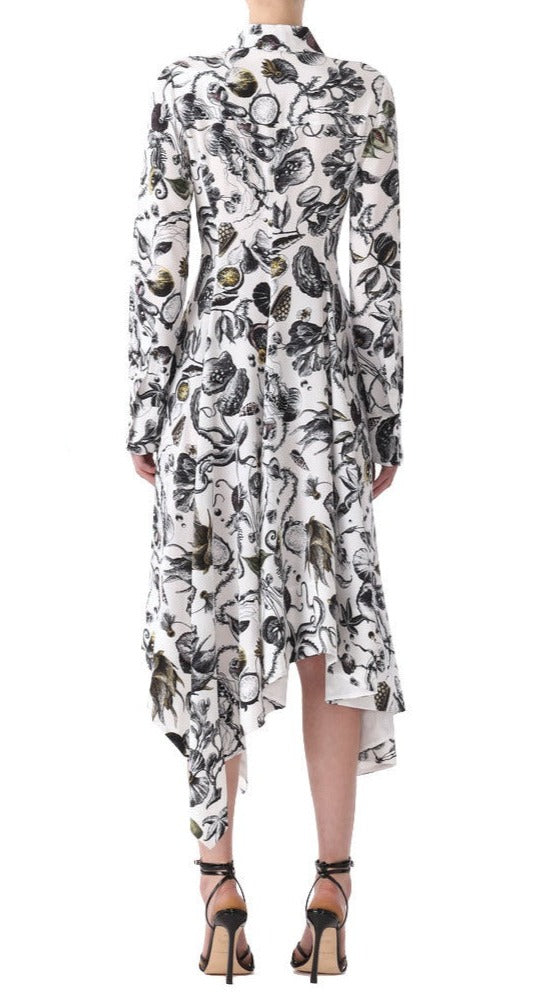 Woman in a Jason Wu Collection Asymmetric Silk Dress with a black and gold floral pattern, standing facing away. The dress has long sleeves and a flowing hem. She is wearing strappy black heels.