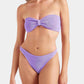 A woman wearing the Hunza G Jean Bikini—a textured, crinkle-fabric bandeau top in lilac with matching high-cut bottoms—stands against a plain white background.