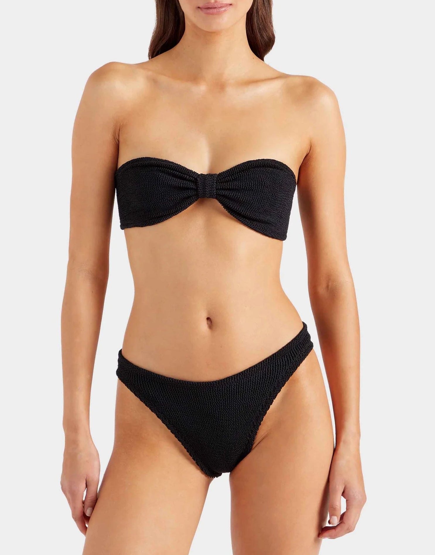 A woman wearing the Hunza G Jean Bikini, featuring black crinkle fabric, stands against a plain light background.