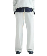 A person wearing TWP PJ Pant—loose-fitting, light gray French terry wide-leg pants with a drawstring—paired with a dark shirt, light top, and dark shoes stands against a white background.