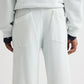 A person is shown from behind wearing TWP's PJ Pant—light-colored, wide-leg pants with two large back pockets, paired with part of a matching top and visible dark shirt cuffs.