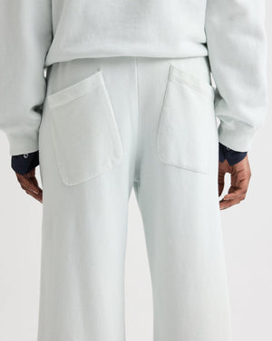 A person is shown from behind wearing TWP's PJ Pant—light-colored, wide-leg pants with two large back pockets, paired with part of a matching top and visible dark shirt cuffs.