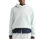 A person wearing a light-colored TWP french terry pullover Hoodie over a dark shirt and light pants, shown from shoulders to waist.