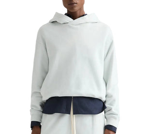 A person wearing a light-colored TWP french terry pullover Hoodie over a dark shirt and light pants, shown from shoulders to waist.